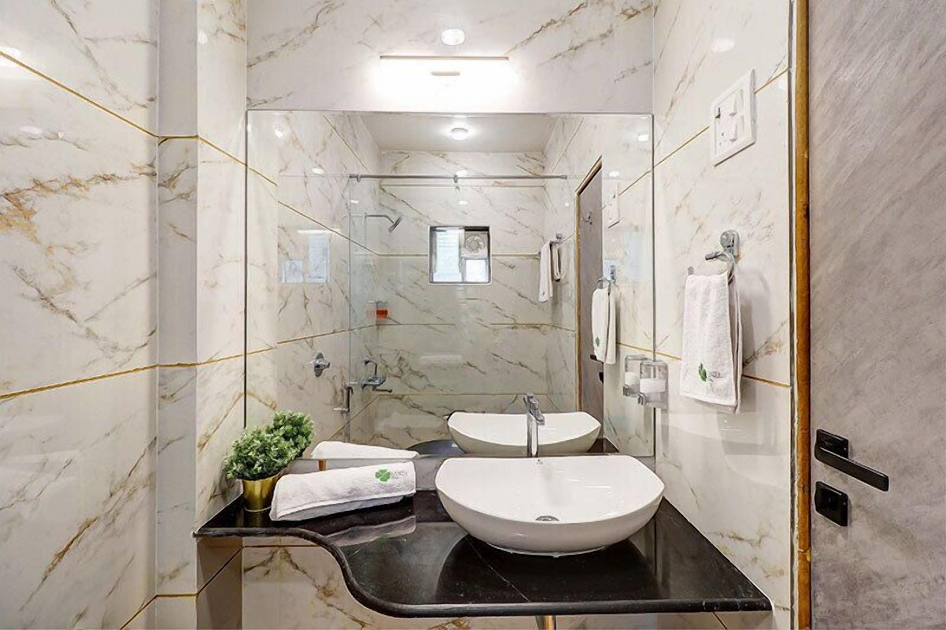 Une salle de bain moderne avec des murs en marbre, deux lavabos, une douche en verre et une petite fenêtre.
