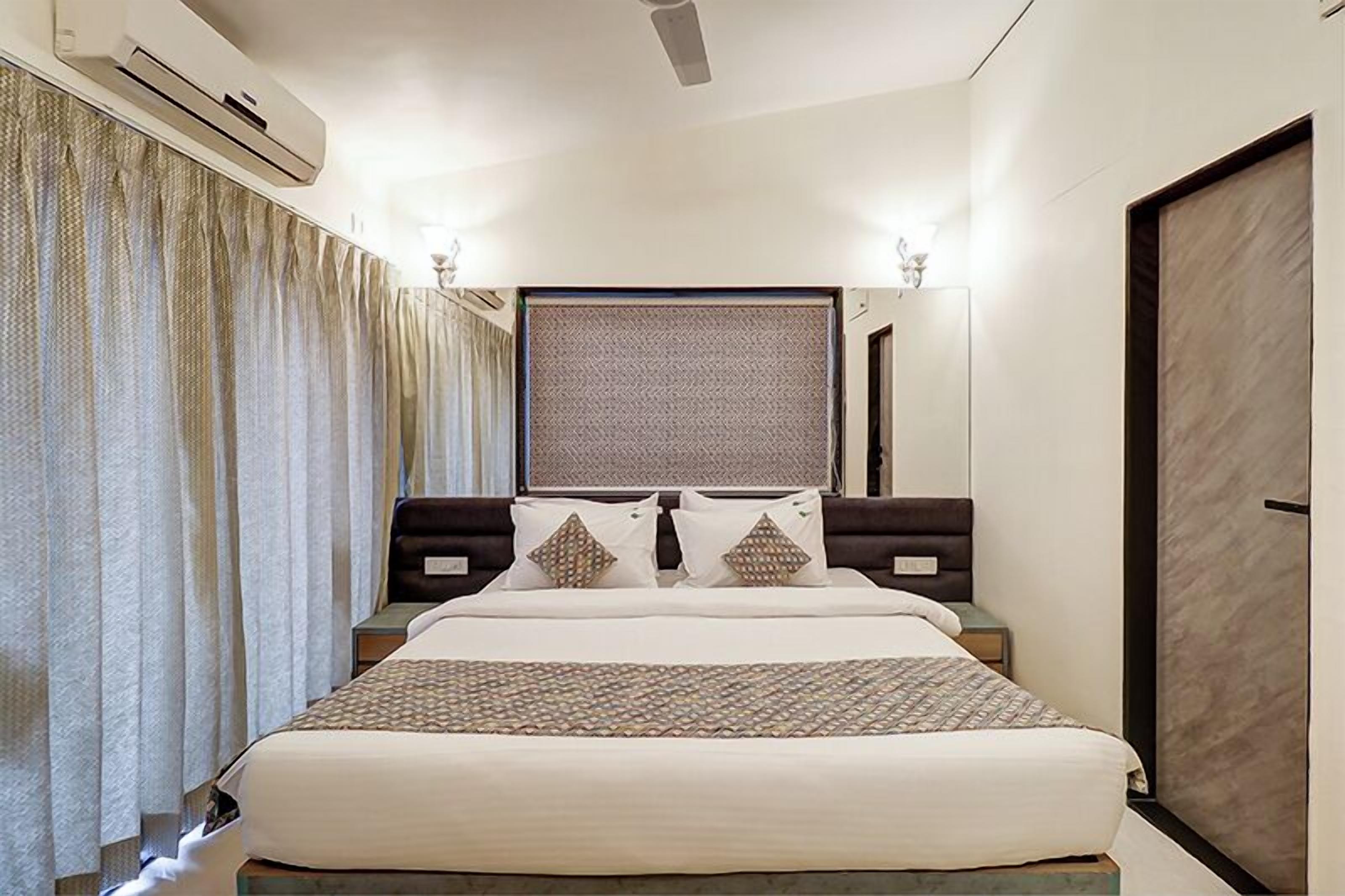 A hotel room with a large bed, a window with curtains, an air conditioning unit, and a mirror.