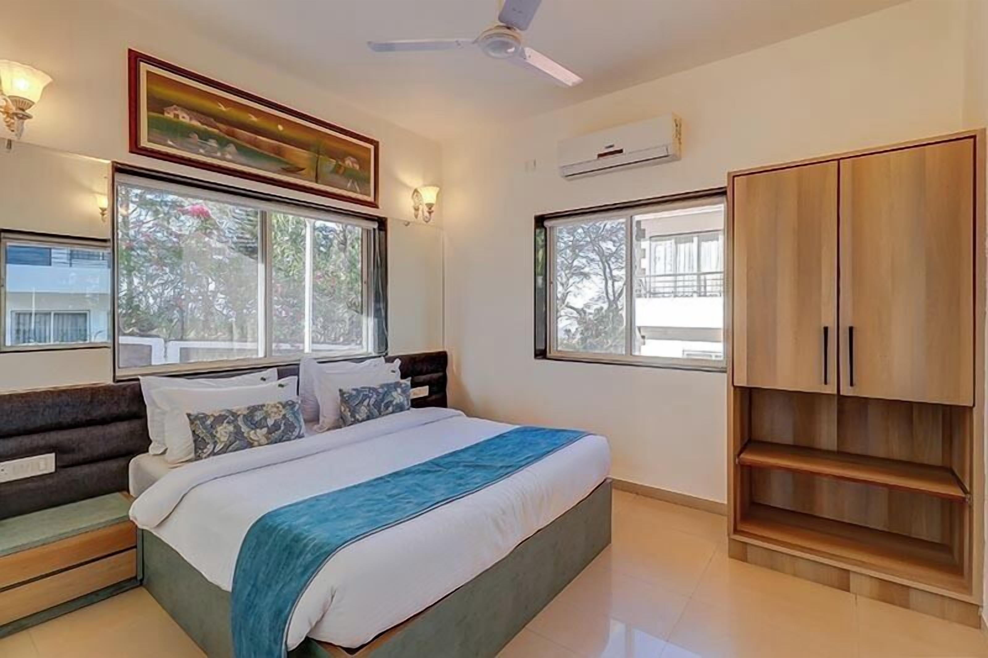 Une chambre à coucher avec un lit, une armoire, un ventilateur de plafond et de grandes fenêtres.