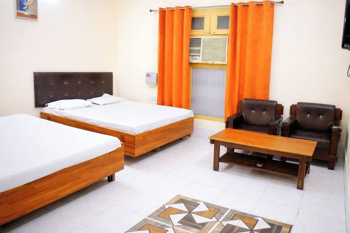 A hotel room with two wooden beds, a sofa, a coffee table, and an air conditioning unit.