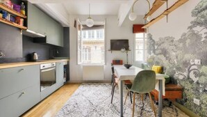 Een keuken met houten kastjes, een eettafel met stoelen, een vloerkleed en een muur met een muurschildering van een boom.