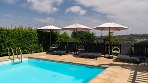 A swimming pool with lounge chairs and umbrellas, surrounded by greenery. - Holiday Home 'Jasmim' with Mountain View, Wi-Fi and Air Conditioning (Guimarães)