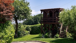Una torre de fusta amb escala, envoltada de vegetació exuberant i un camí empedrat.