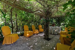 Un espace extérieur aménagé avec des chaises et des tables jaunes, entouré de verdure et agrémenté d’une pergola.