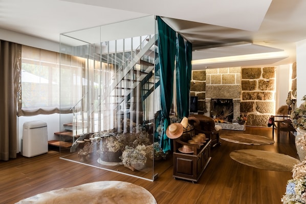 Un salon moderne avec une cloison en verre, une cheminée en pierre et un escalier en bois.