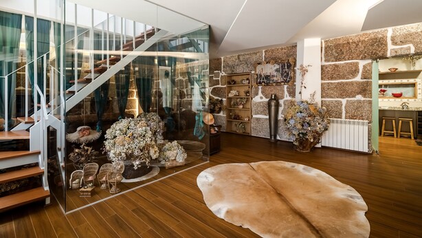 Un interior modern amb una escala de vidre, terres de fusta i una paret de pedra.