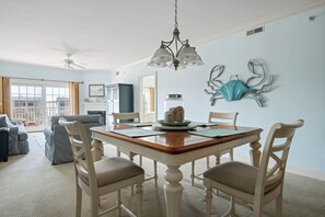 A dining area with a wooden table, white chairs, a chandelier, and a decorative wall piece. - Charming retreat on 14th Street overlooking the canal White Marlin Open takes place, close to the beach and boardwalk (Ocean City)