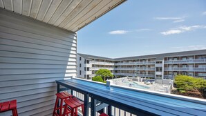 Ein Balkon mit Blick auf einen Pool, rote Barhocker und ein blauer Tisch.