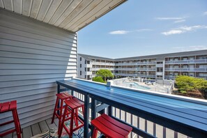 A balcony with a pool view, red bar stools, and a blue table. - Two bedroom mid-town condo with a pool! (Ocean City)