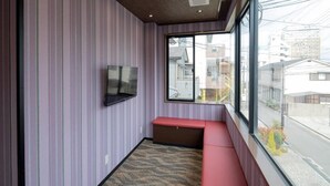 Ein Zimmer mit Streifenmuster an der Wand, einer Bank, einem Flachbildfernseher und einem großen Fenster mit Blick auf Gebäude.