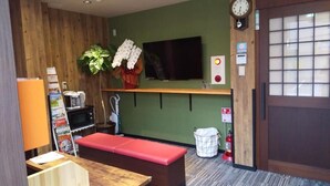 Ein Zimmer mit einer hölzernen Bank, einem Fernseher, einer Pflanze, einem Feuerlöscher und einer Wanduhr.