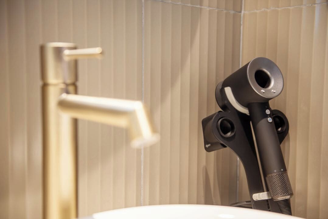 A bathroom with a modern faucet and a black hairdryer mounted on the wall.