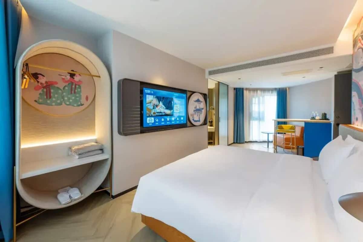 A hotel room with a bed, a TV, a wall-mounted shelf, and a circular seating area.
