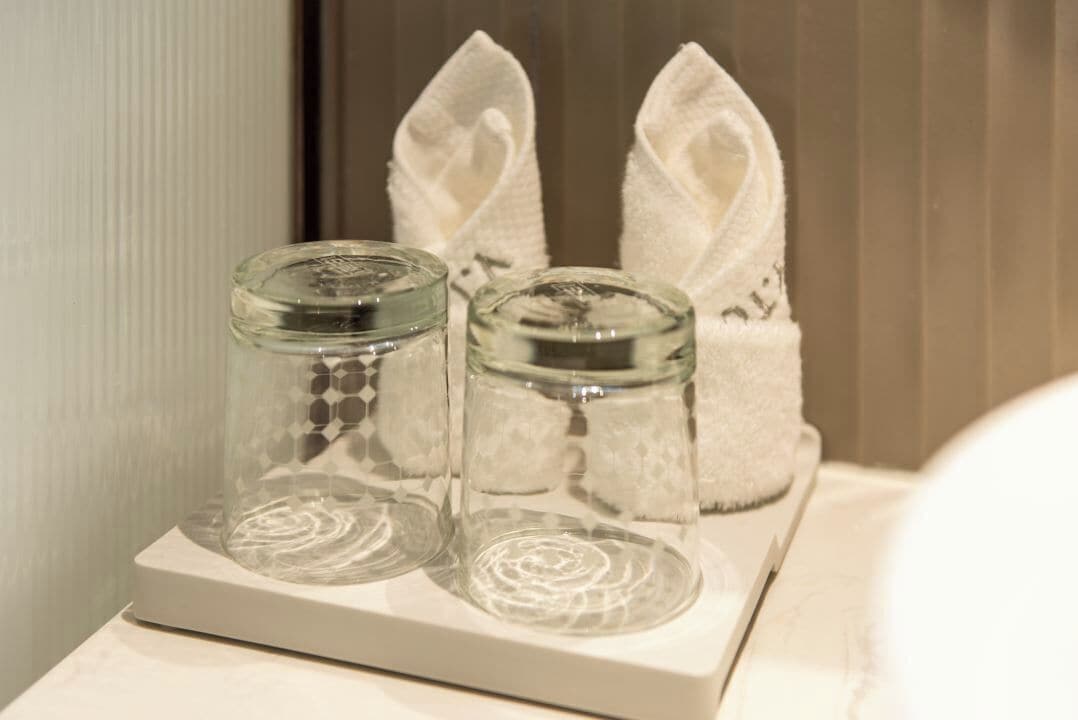 Ein Badezimmer mit zwei Glasbehältern auf einer weißen Ablage, einem weißen Handtuch und einer weißen Badmatte.