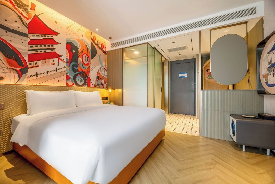 A hotel room with a large bed, a wall with a colorful mural, a mirror, and a washing machine.