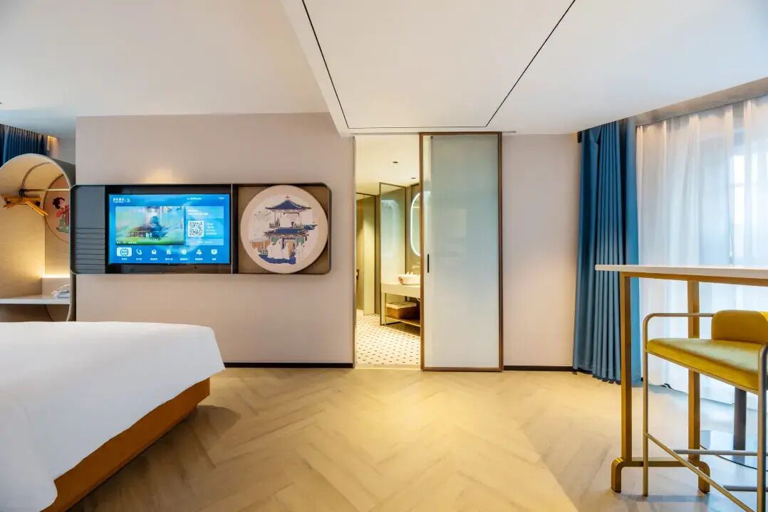 Een hotelkamer met een bed, een aan de muur bevestigde televisie, een bureau met stoel en een schuifdeur naar een badkamer.