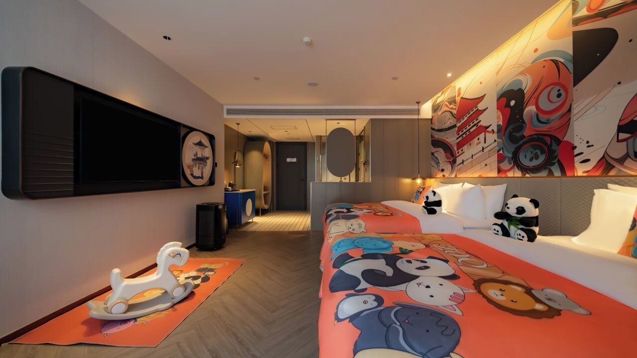 Een hotelkamer met een bed, een televisie, een bank, een beddegoed met een panda-print en een muur met een muurschildering.