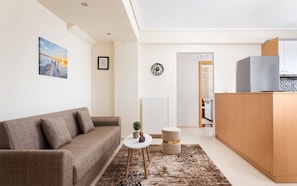 A modern living room with a sofa, a small round table, a clock, and a view into the kitchen.