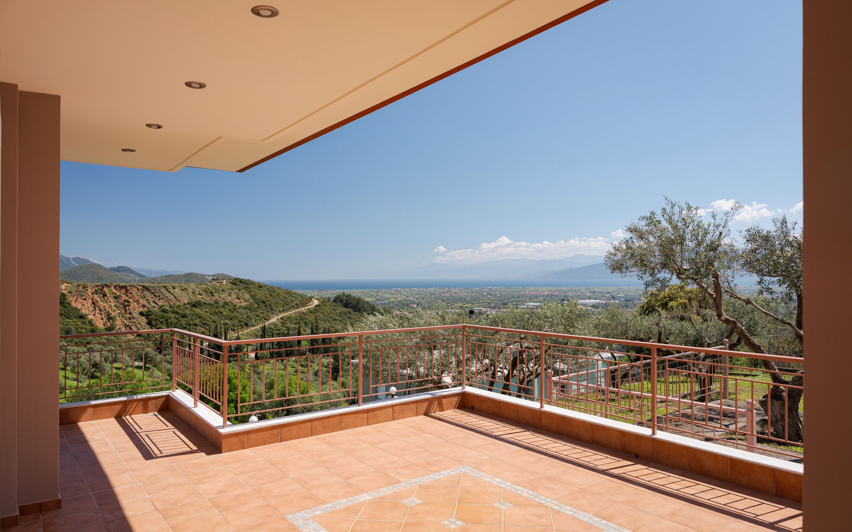 A balcony with a metal railing, terracotta tiles, and a view of a mountainous landscape.