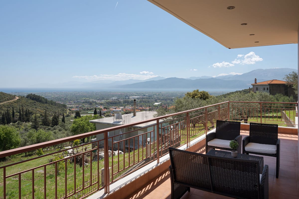A balcony with wicker furniture, a view of a valley, and distant mountains.
