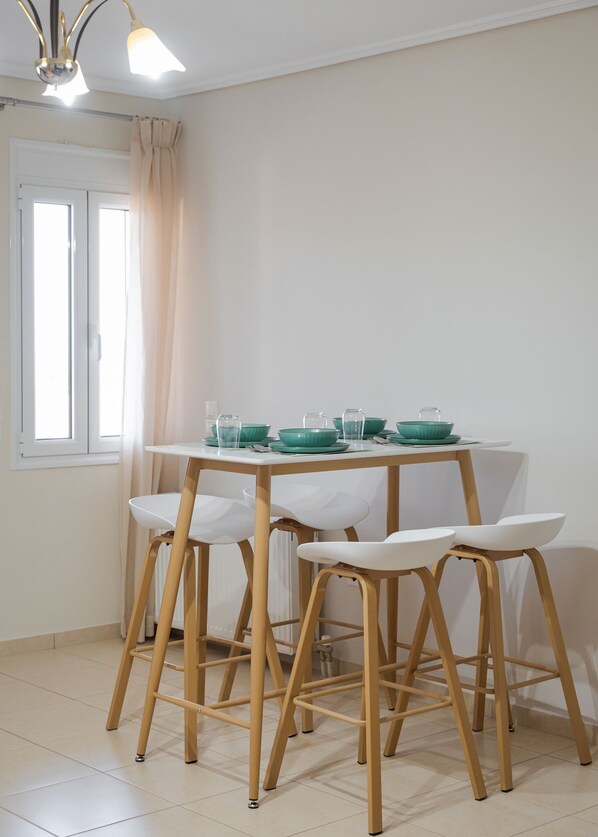 Un coin repas avec une table dressée pour quatre personnes, des chaises en bois et une fenêtre avec des rideaux.