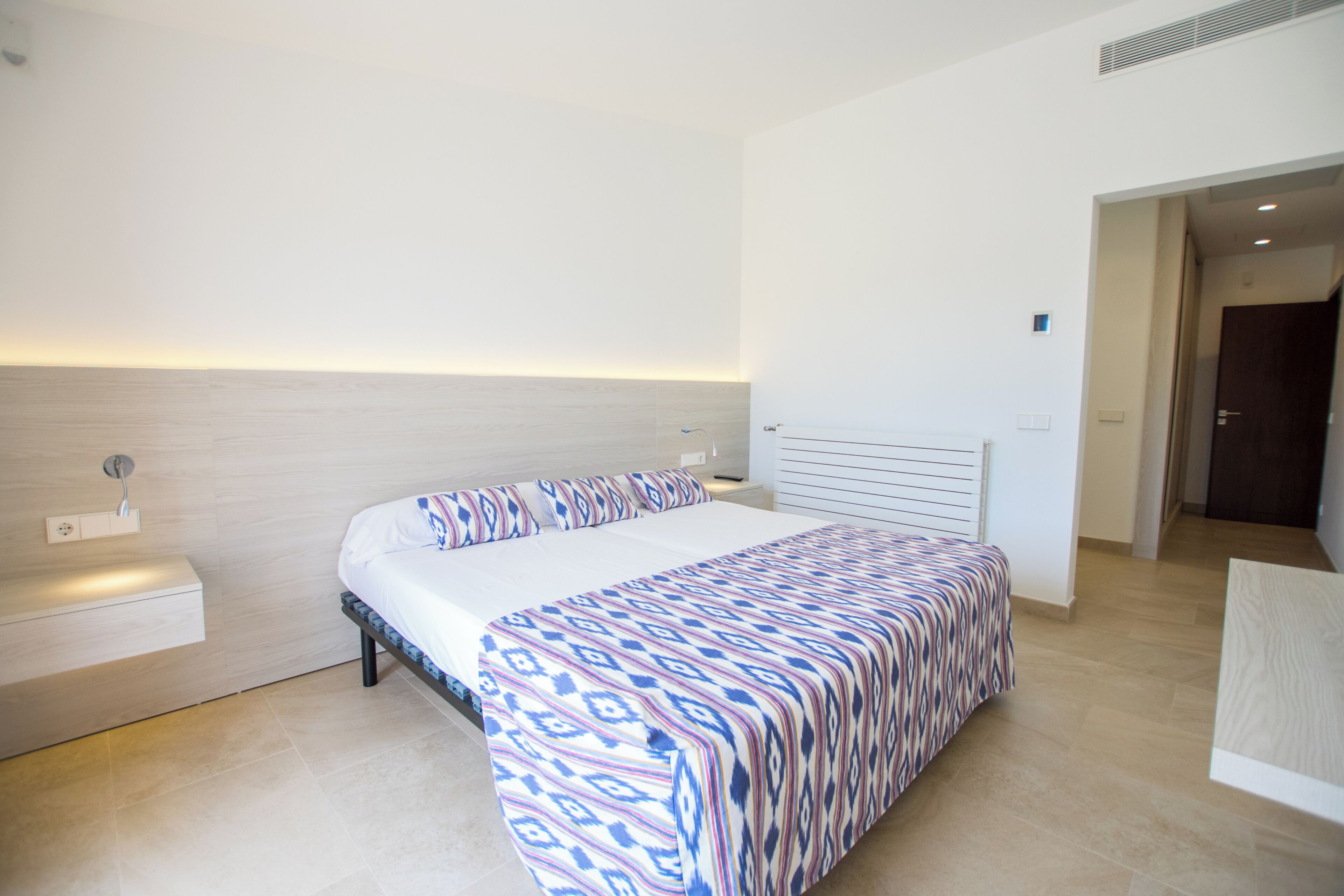 A modern hotel room with a large bed, bedside table, and a view of the sea.