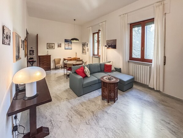 A living room with a sofa, a small round table, a lamp, and a dining area with chairs and a table. - Maison Faber - Apartment in Pisa (Pisa)
