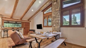 Un comedor acogedor con una mesa de madera dispuesta para cuatro, una pared de piedra decorativa y un ventanal con vistas al verdor.