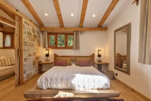 Ein Schlafzimmer mit einem großen Bett, Holzbalken, einer Steinwand und einem Spiegel.