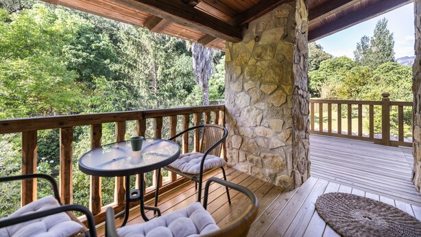 Una terraza de madera con un pilar de piedra, una mesa redonda y dos sillas con cojines.
