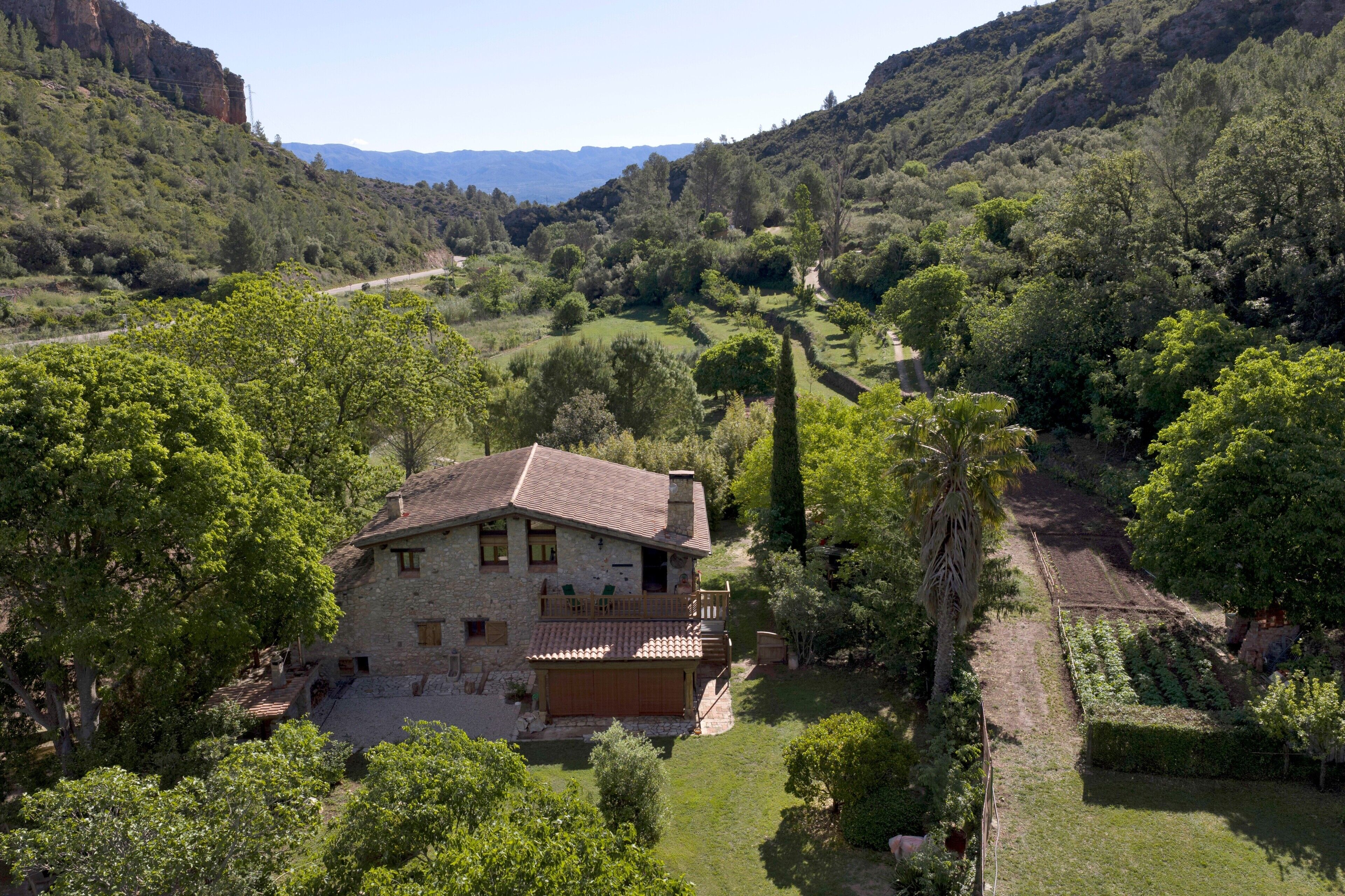 A stone house with a balcony, surrounded by lush greenery and hills.