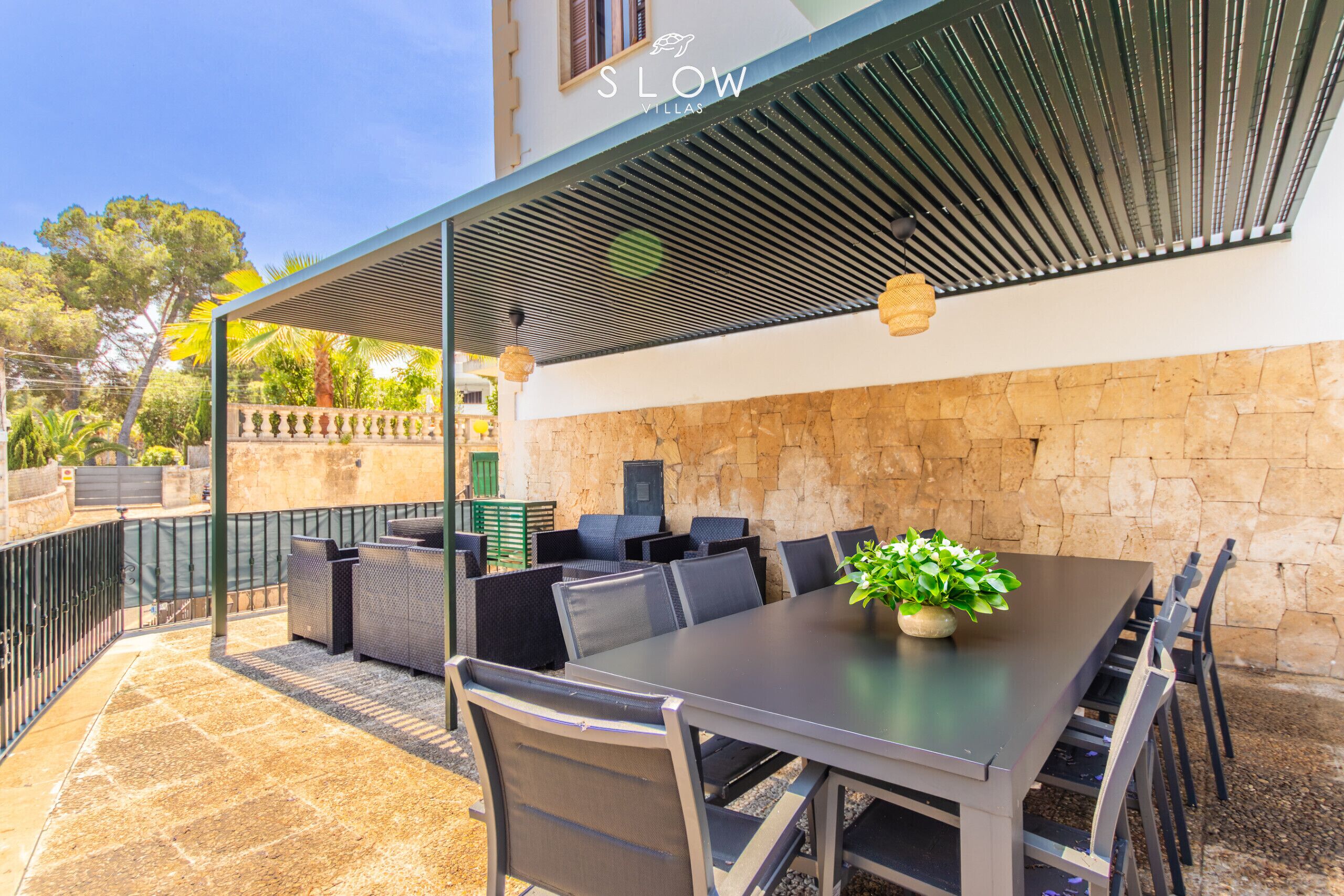 Une terrasse extérieure avec une table et des chaises, une pergola et un mur en pierre.