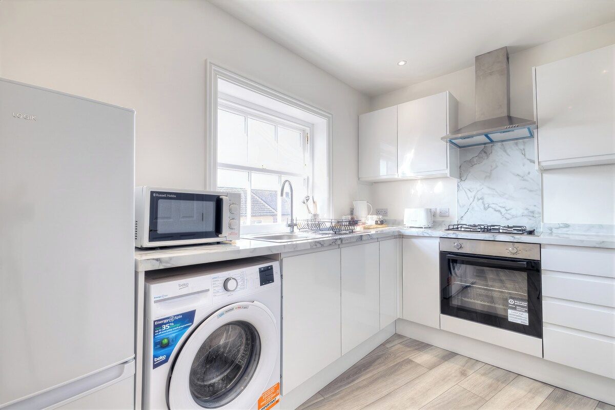 A modern kitchen with a washing machine, microwave, stove, and oven.