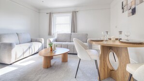 Una sala de estar moderna con un sofá, una mesita de centro y una mesa de comedor lista para dos personas.