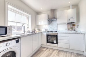Une cuisine moderne avec des meubles blancs, un lave-linge encastré, un four à micro-ondes et une cuisinière.