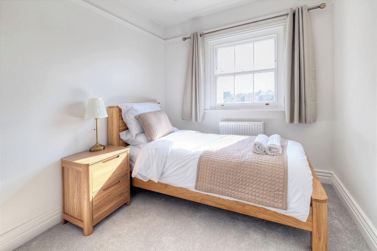 Une chambre à coucher avec un lit en bois, une table de chevet, une lampe et une fenêtre avec des rideaux.