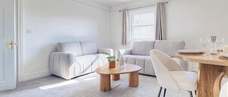 A modern living room with a sofa, a coffee table, and a dining area with a chair and table.