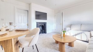 Una sala de estar moderna con chimenea, un sofá, una mesa de comedor con sillas y un televisor de pantalla plana montado en la pared.