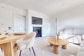 Un salon moderne avec une cheminée, un canapé, une table à manger avec des chaises et un téléviseur à écran plat fixé au mur.