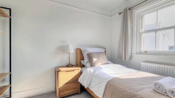 A bedroom with a bed, bedside table, lamp, and a window with curtains.