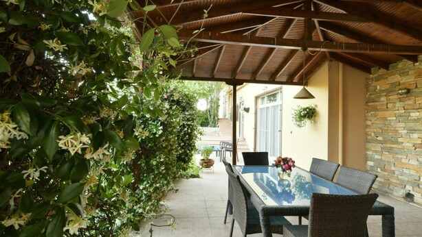Un patio al aire libre con una zona de estar cubierta, una mesa y sillas, y un muro de piedra.