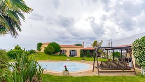 Un patio trasero con piscina, un columpio de madera y una casa con techo rojo.
