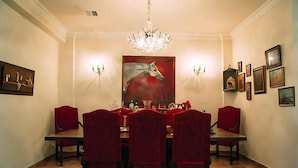 Un comedor con candelabro, sillas tapizadas en rojo, un cuadro grande y apliques de pared.
