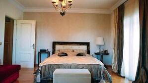 Un dormitorio con una cama grande, una mesita de noche, una lámpara, una silla roja y una puerta.