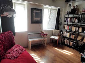 A living room with a red sofa, a bench, a chair, a bookshelf, and a window with blinds.