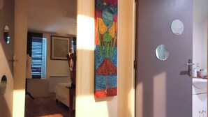 Un couloir avec un tableau, une porte avec un miroir et une fenêtre avec des stores.