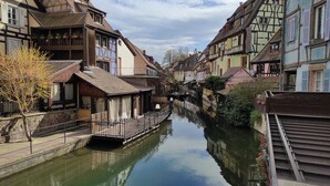 Un étroit canal bordé de bâtiments traditionnels à colombages, d’un pont en bois et d’une enseigne de restaurant.