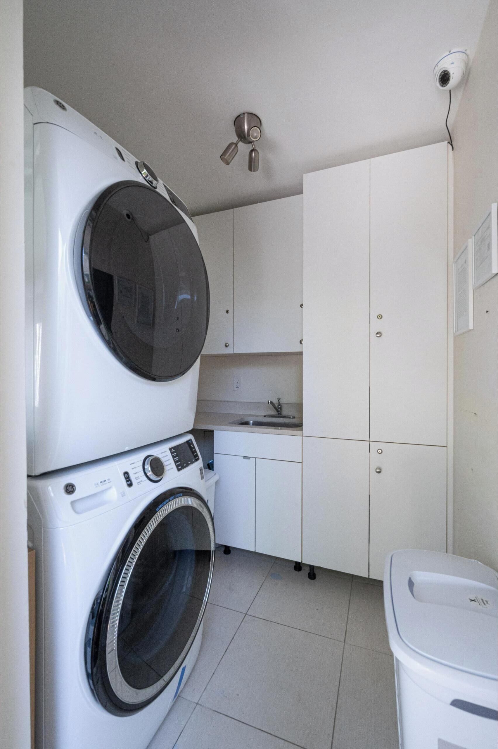 A laundry area with stacked washers and dryers, a sink, and a security camera.