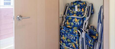 Una stanza con una porta di legno, una sedia bianca e una carrozzina blu con motivo tropicale.