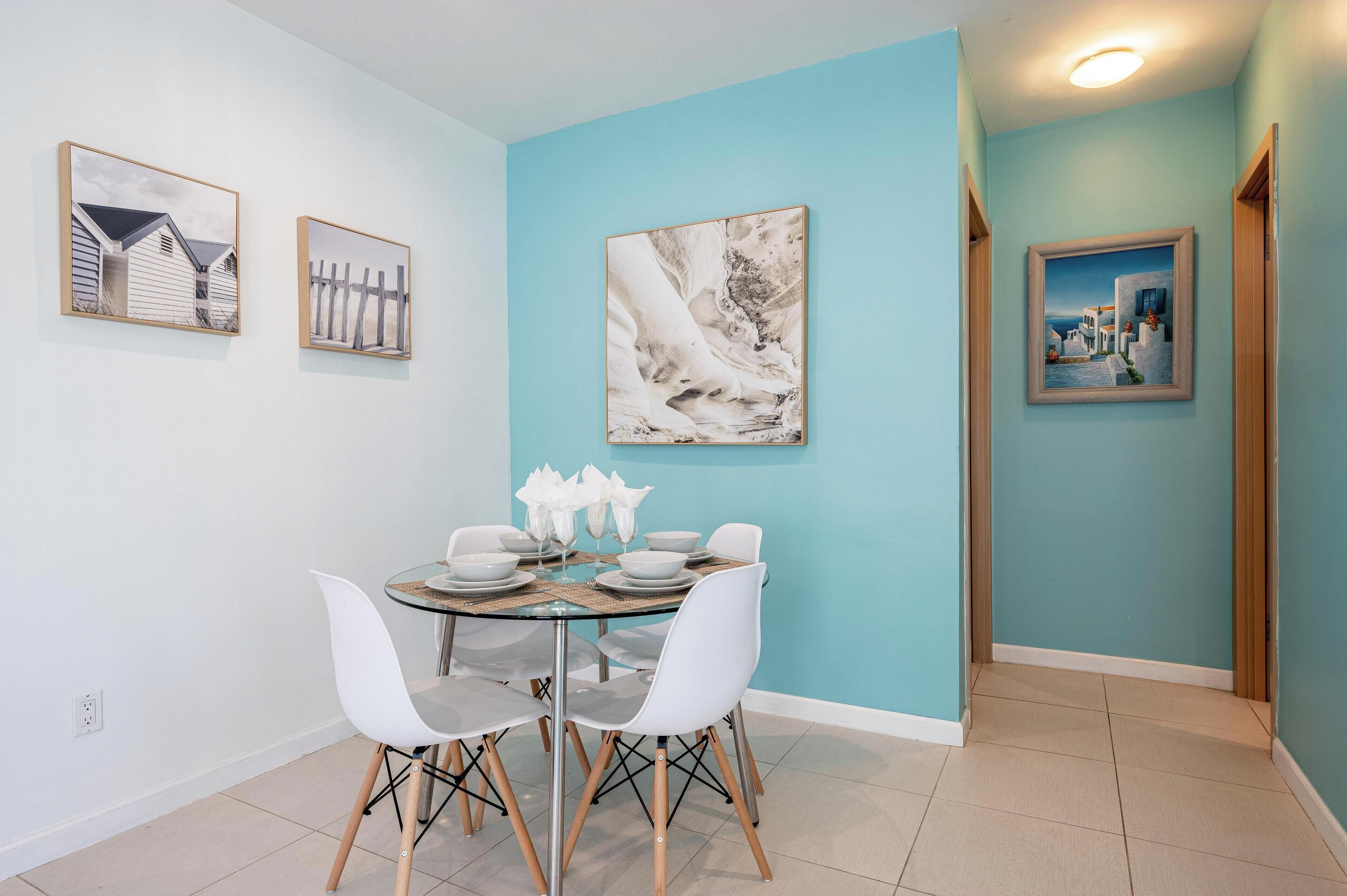 A dining area with a round table, white chairs, and a blue wall with artwork.